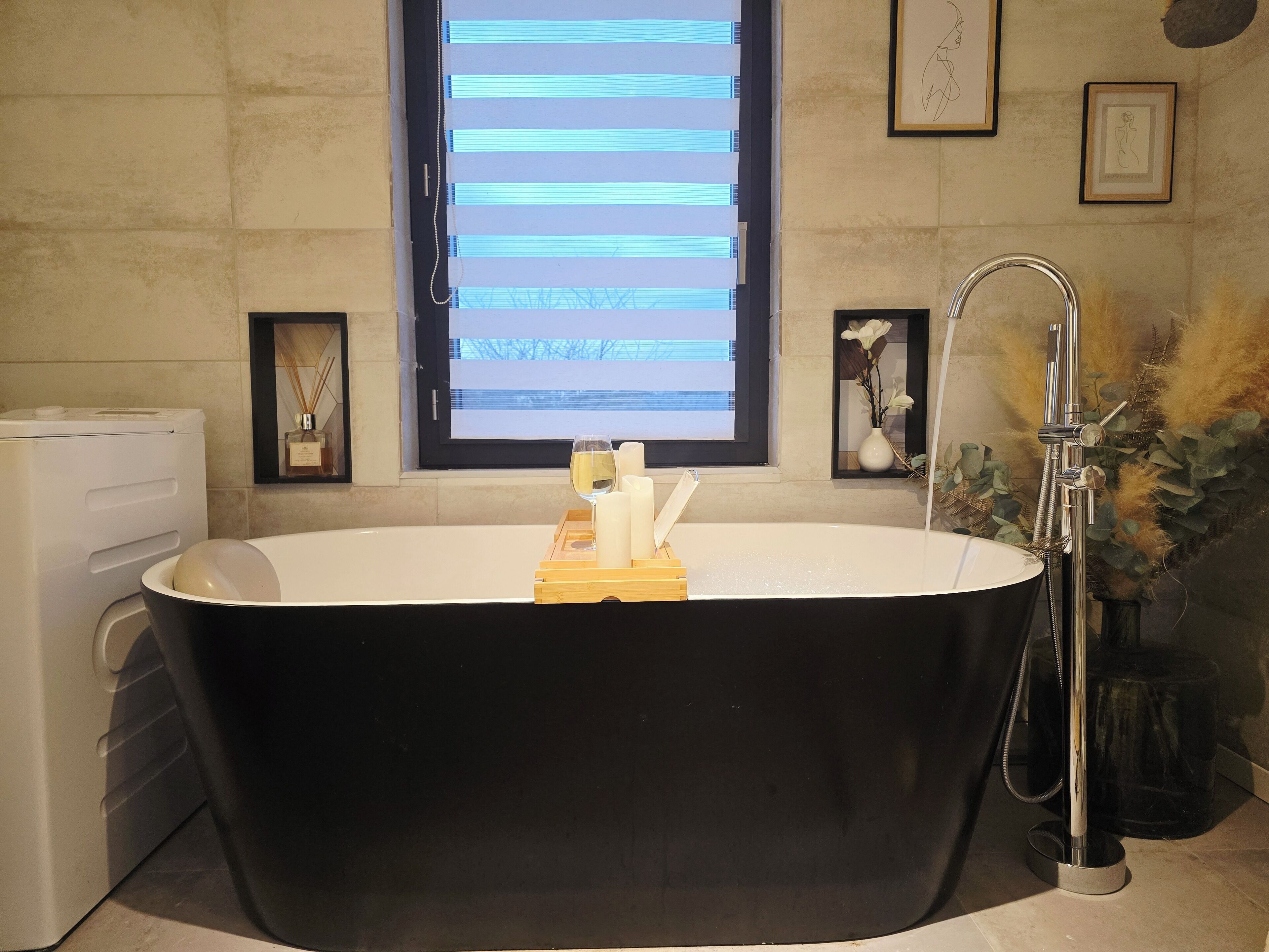 Un baño moderno con una bañera independiente, una ventana con persianas horizontales y una obra de arte enmarcada en la pared.