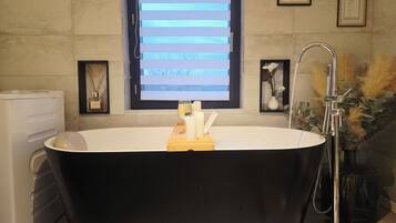 Un baño moderno con una bañera independiente, una ventana con persianas horizontales y una obra de arte enmarcada en la pared.