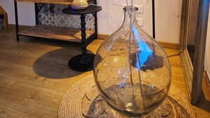 A room with a wooden floor, a glass vase with feathers, a lamp, a bookshelf, and a mirror.