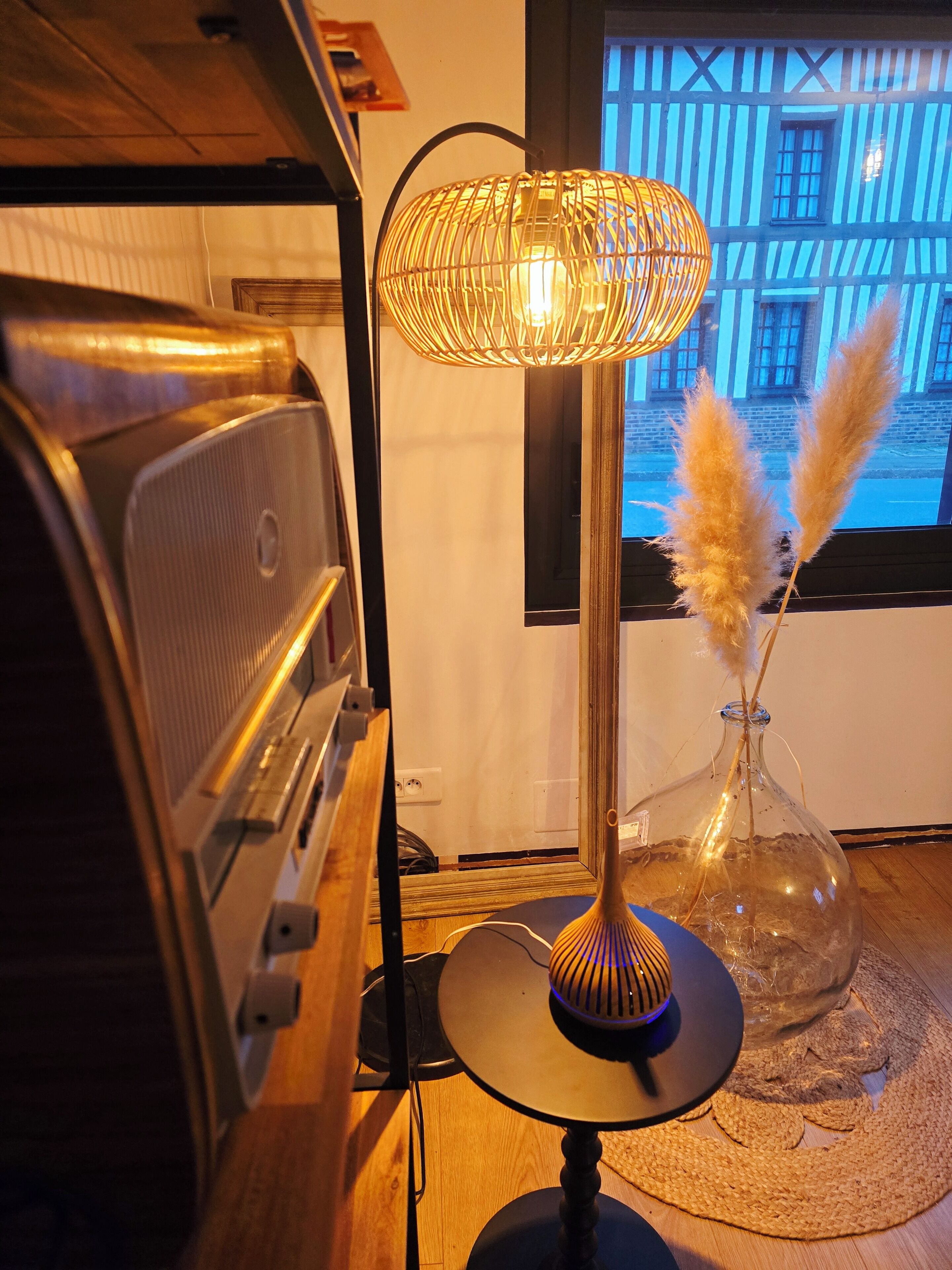 Ett rum med en gammal radio, en modern lampa och en vas med pampasgräs.