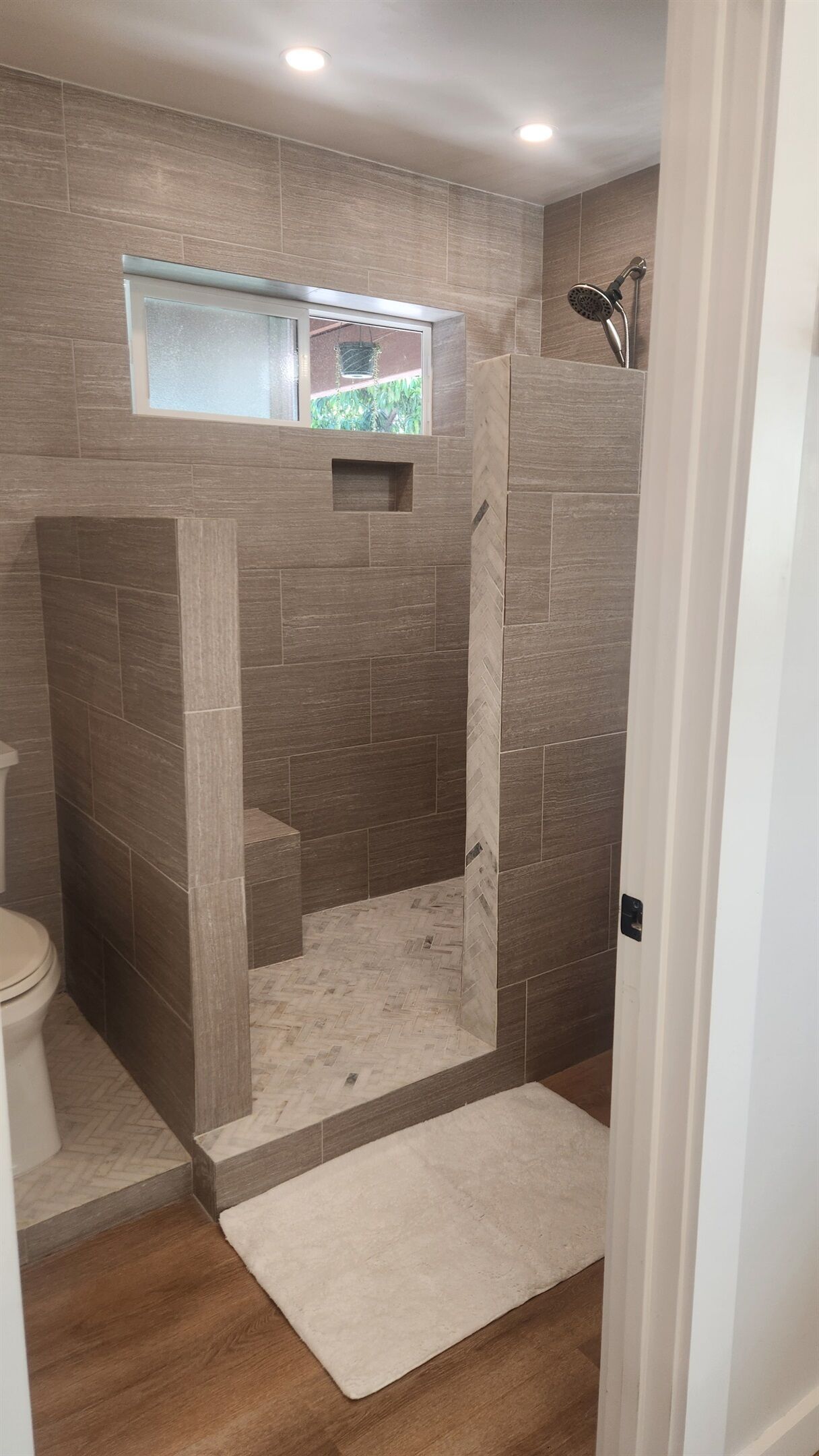 A bathroom with a shower, a toilet, and a small window.