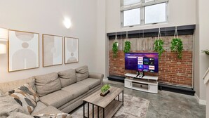 Een moderne woonkamer met een grijze bank, een salontafel en een flatscreen televisie die aan een bakstenen muur is bevestigd.