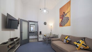 Een compacte woonruimte met een bank, een flatscreen televisie, een eettafel met stoelen en een schilderij aan de muur.