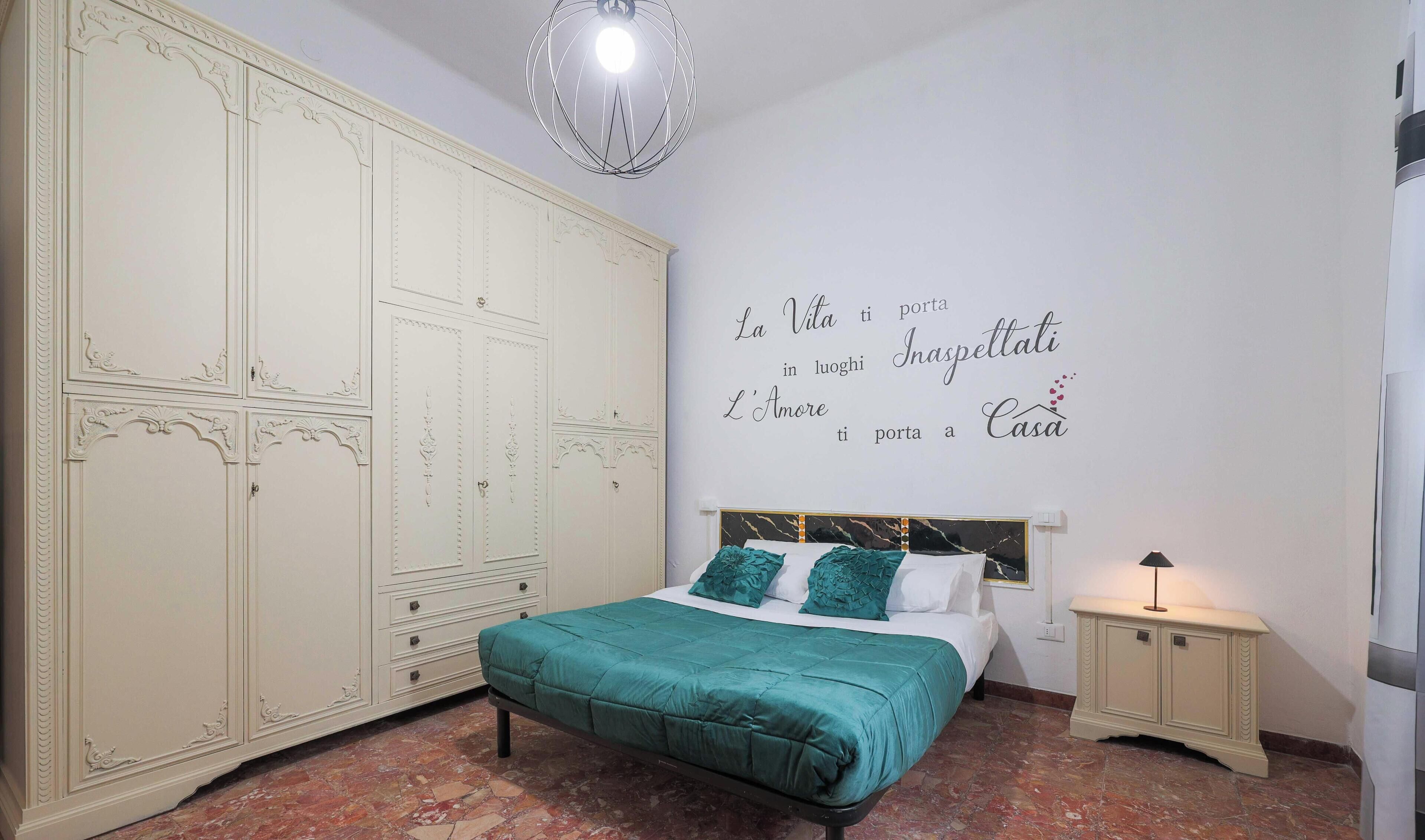 Un dormitorio con cama, armario, una pared con una cita motivacional y una mesita de noche.