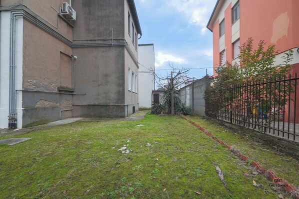 Une cour intérieure avec une pelouse, une clôture en métal noir et des bâtiments présentant un mélange de styles architecturaux.
