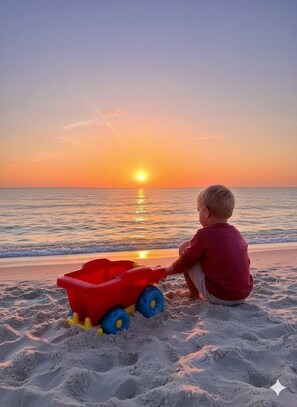 A child playing with a red toy truck on a beach at sunset. - 3-bedroom house in perfect Yarmouth with cool AC breeze (Yarmouth)