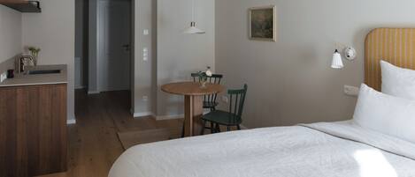 Ett sovrum med en säng, ett skrivbord, en stol och ett litet bord med en vas.