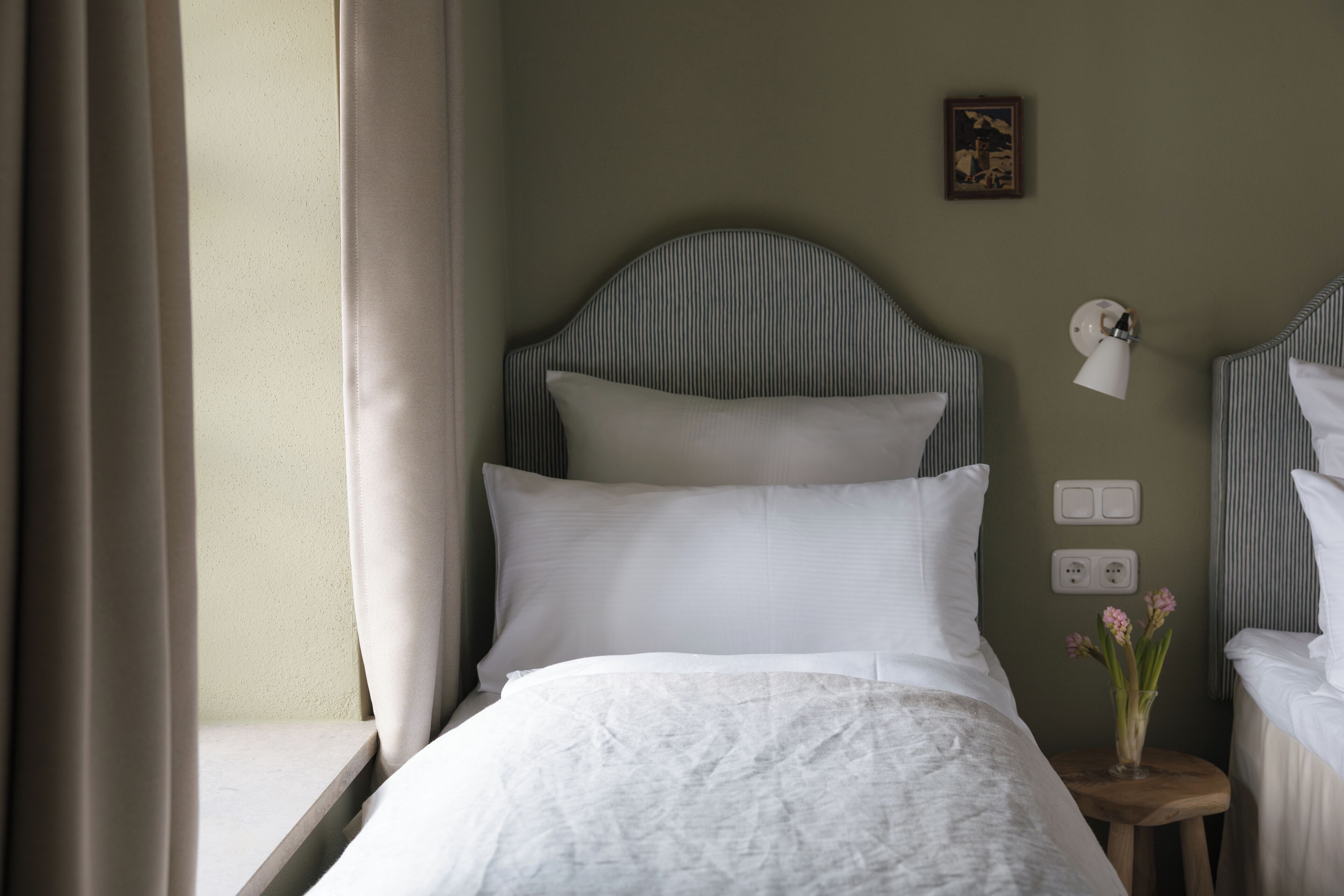 A neatly made bed with white linens, a striped headboard, and a bedside table with a lamp and flowers.