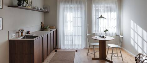 A modern kitchen with a wooden island, a dining area with a round table and chairs, and a large window with sheer curtains.