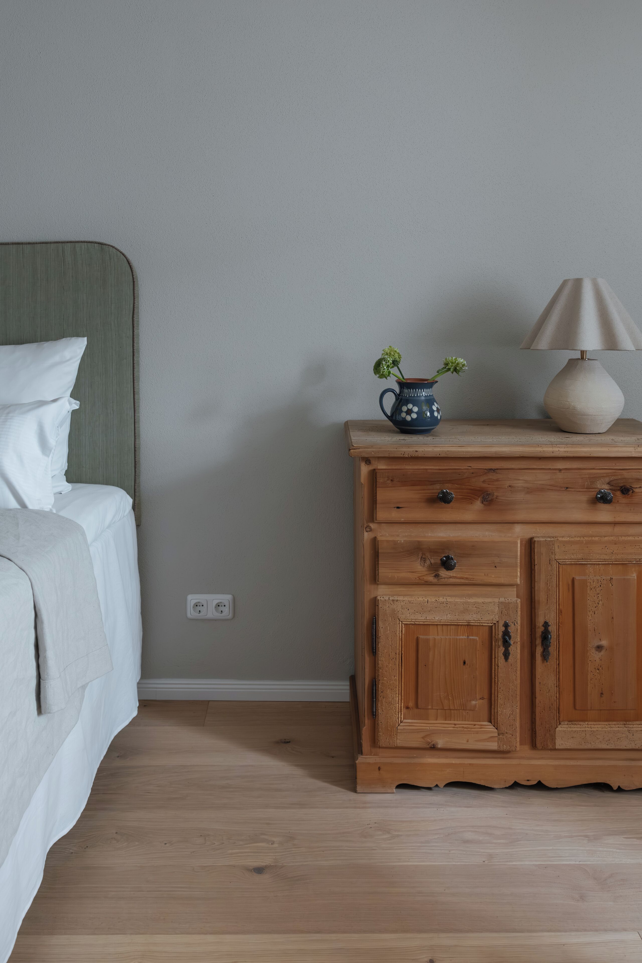 Une chambre à coucher avec un lit, une commode en bois, une lampe et un vase rempli de fleurs.