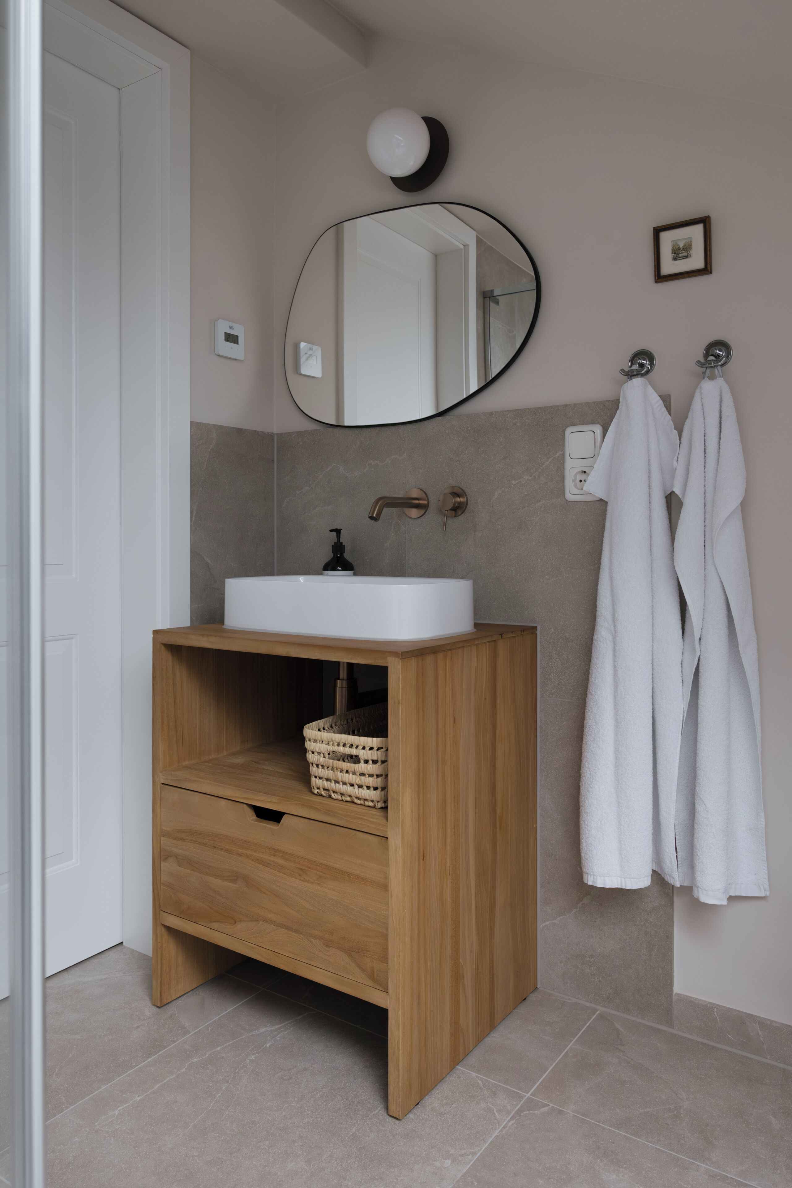 A bathroom with a wooden vanity, a white sink, a mirror, and two white towels hanging on hooks.