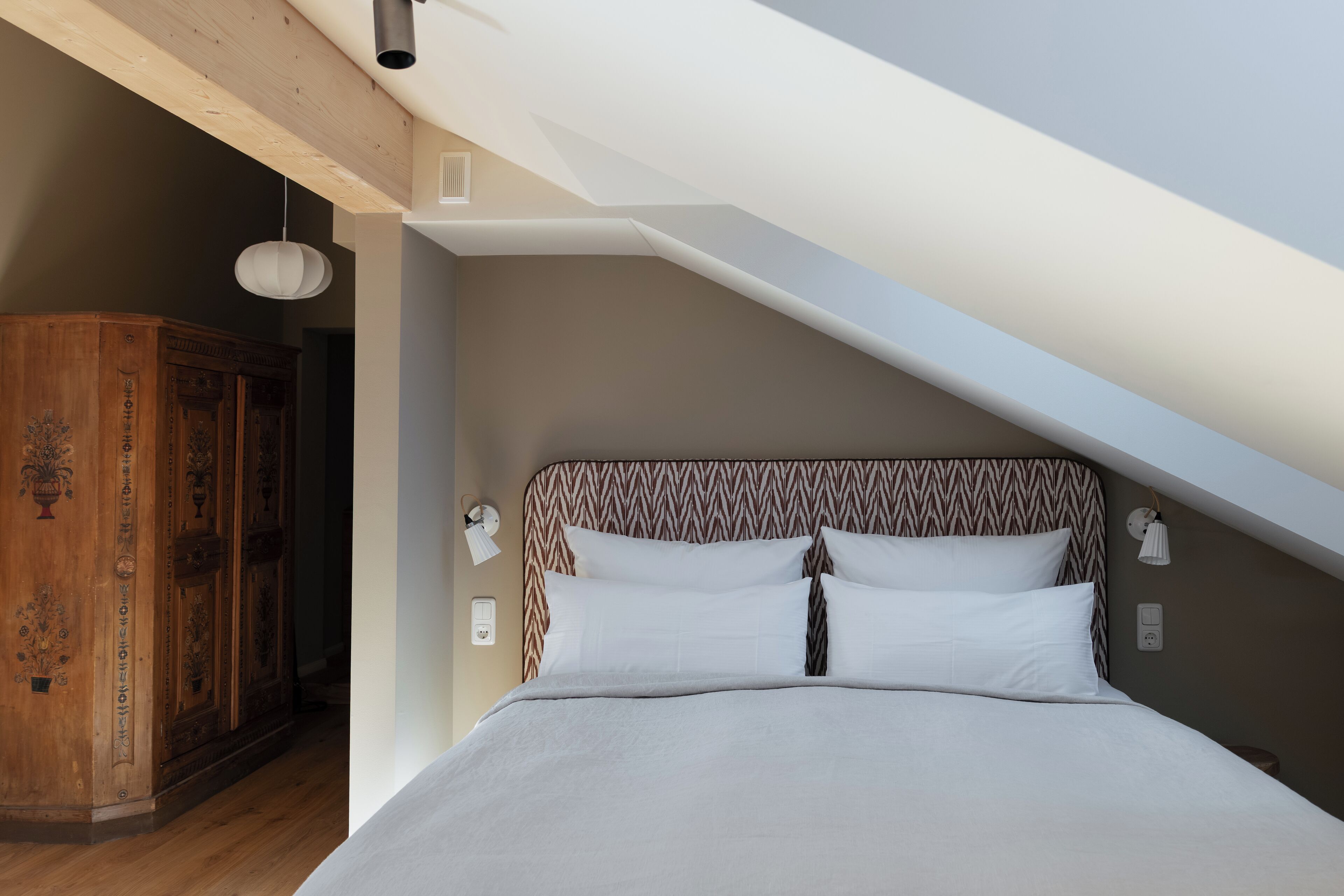 A bedroom with a bed, wooden wardrobe, and a sloped ceiling.