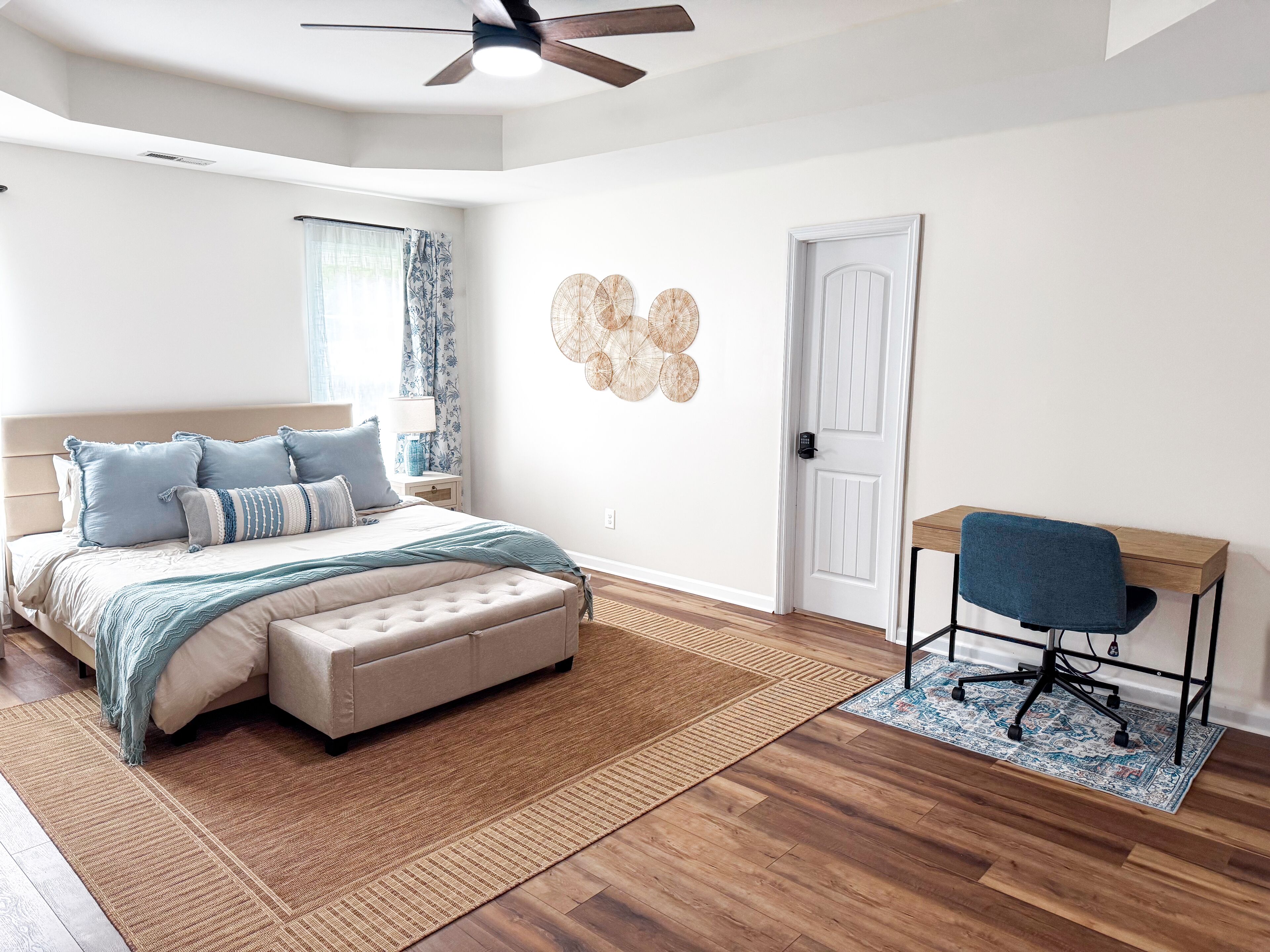 A bedroom with a bed, a desk, a chair, a ceiling fan, and a door.