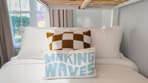 Una cama con ropa de cama blanca y una almohada con el texto 'MAKING WAVES'.