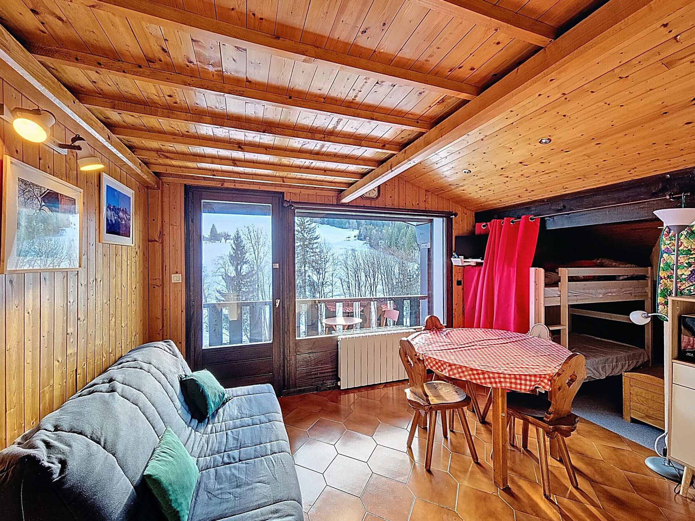L’intérieur chaleureux d’un chalet avec un plafond en bois, un canapé, une table à manger avec des chaises et un lit superposé.