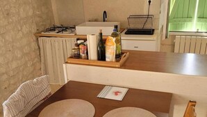 A kitchen with a wooden table, two woven placemats, a bottle of olive oil, and a bottle of vinegar on the counter. - Charming Old House near Chinon with Private Courtyard (Tavant)
