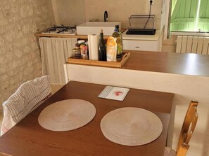 A kitchen with a wooden table, two woven placemats, a bottle of olive oil, and a bottle of vinegar on the counter. - Charming Old House near Chinon with Private Courtyard (Tavant)