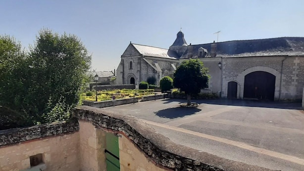 A courtyard with a stone wall, a small tree, and a building with a pointed roof. - Charming Old House near Chinon with Private Courtyard (Tavant)