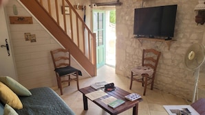 A cozy living room with a wooden staircase, a flat-screen TV, a fan, and a coffee table with books. - Charming Old House near Chinon with Private Courtyard (Tavant)
