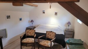 A bedroom with a bed, two chairs, a nightstand, a lamp, and a small window. - Charming Old House near Chinon with Private Courtyard (Tavant)