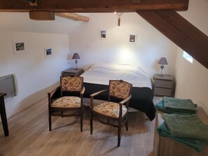 A bedroom with a bed, two chairs, a nightstand, a lamp, and a small window. - Charming Old House near Chinon with Private Courtyard (Tavant)