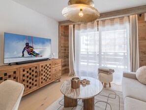 A modern living room with a television, wooden furniture, a round coffee table, and a large window with curtains. - New residence, ski-in, Huez center, 2 adults + 4 children (Huez)