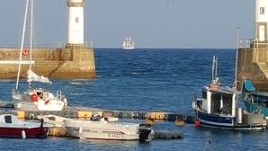 En hamn med båtar förtöjda nära en fyr, en segelbåt i fjärran och en klar himmel.