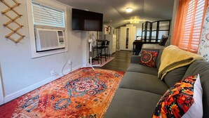 Un salón con sofá, alfombra estampada y televisor montado en la pared.