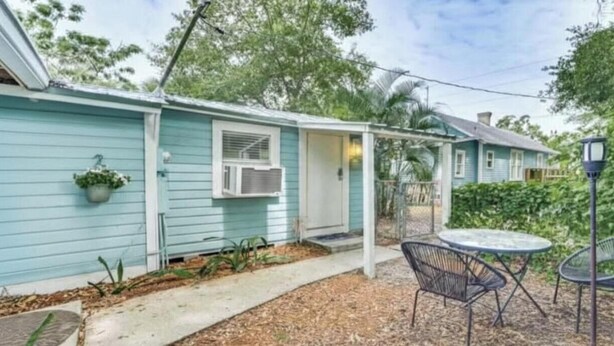 Una casa azul claro con un porche cubierto, mobiliario exterior y un pequeño jardín.
