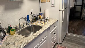 Una cocina con encimera de granito, pileta de acero inoxidable, alacenas blancas y un refrigerador.