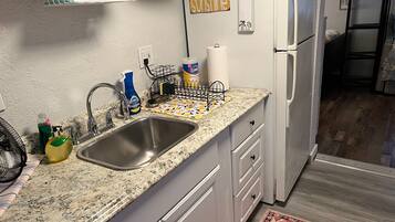 A kitchen with a granite countertop, stainless steel sink, white cabinets, and a refrigerator.