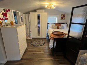 A compact bedroom with a bed, bedside table, wardrobe, and a small kitchen area with a refrigerator and a microwave. - Lakeland Garden Guesthouse (Lakeland)