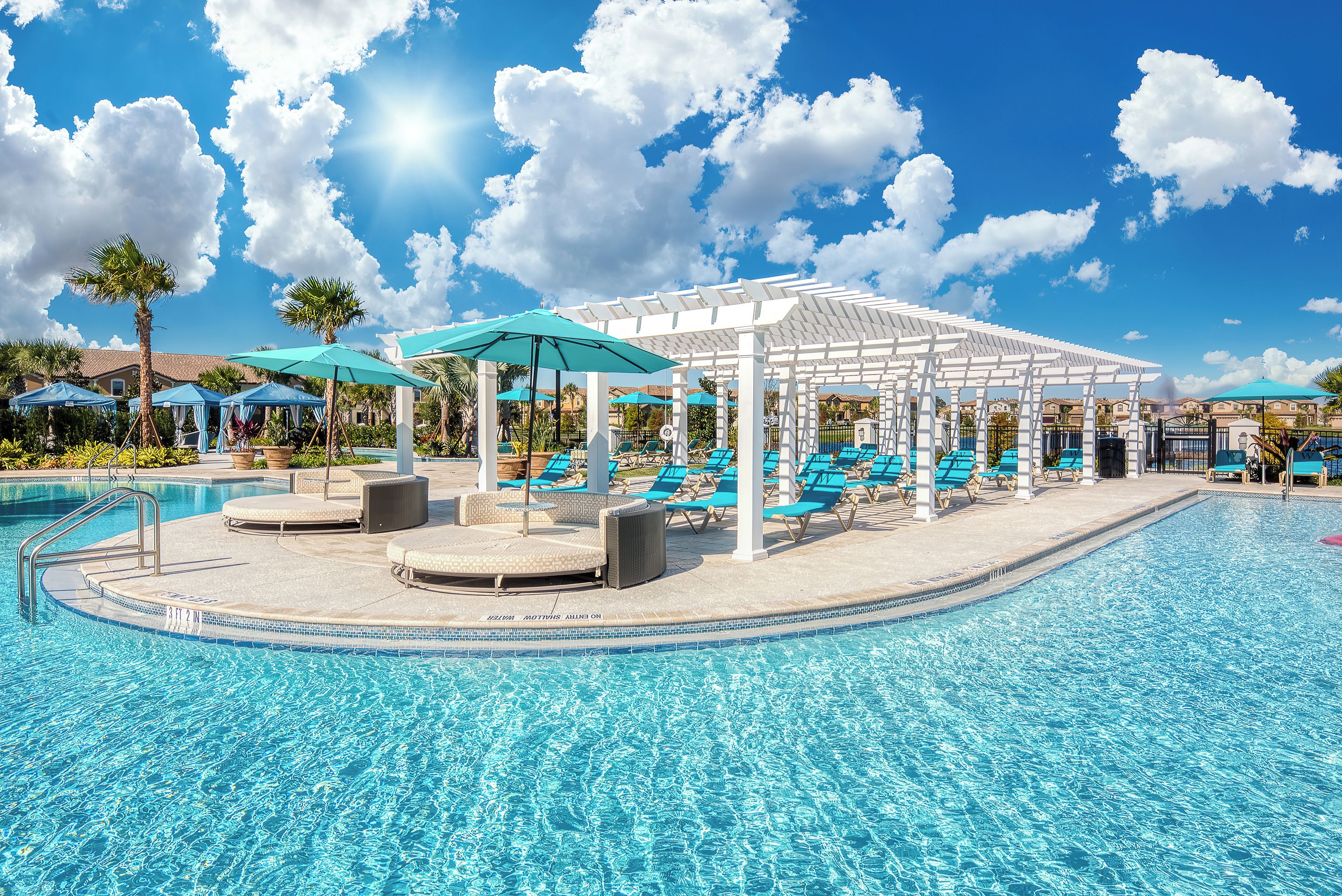 Un espace piscine agrémenté de chaises longues et de parasols, le tout entouré d’une pergola blanche.