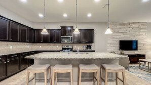 A modern kitchen with dark cabinets, a large island with stools, a microwave, and a built-in TV. - Free Pool Heat+BBQ|Fam Resort|Themed Frozen + Harry Potter|Star Wars Gameroom (Kissimmee)