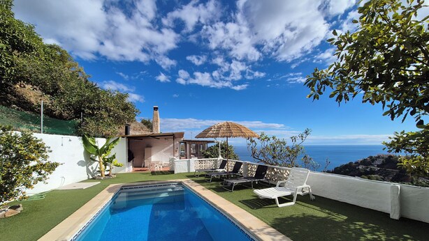 Ein Pool mit Meerblick, ein kleines Haus mit Schornstein und Sitzgelegenheiten im Freien.