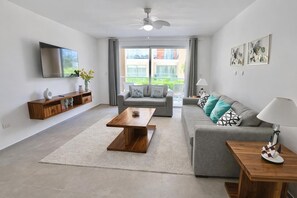 A modern living room with a grey sofa, a wooden coffee table, a grey couch, and a TV mounted on the wall. - Beachfront 2bedRm 2Bath Apt G1-3 PlayaNuevaRomana w/Pool,JacuziSpa,GolfTenis,Gym (Playa Nueva Romana)