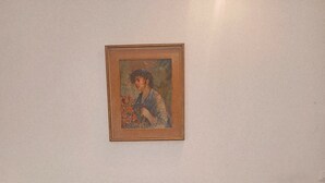 A grey sofa with two blue cushions against a plain wall, with a framed painting above it. - La Casa di Sandhya (Udine)