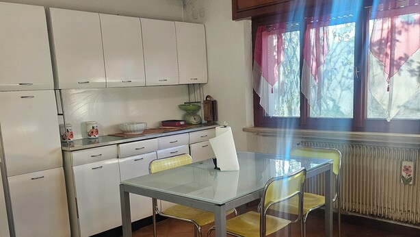 A kitchen with white cabinets, a glass table, and yellow chairs. - La Casa di Sandhya (Udine)