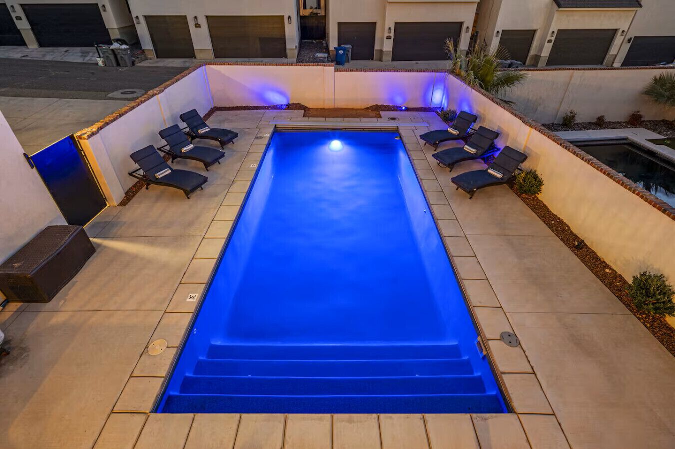 A rectangular swimming pool with a blue tint, surrounded by a tiled deck and equipped with multiple lounge chairs.