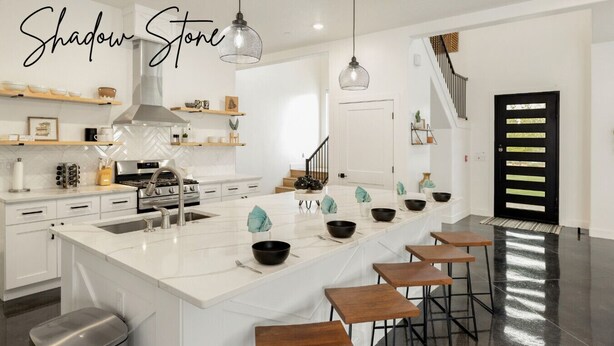 Une cuisine moderne dotée d’un grand îlot central, de tabourets de bar et de luminaires suspendus.