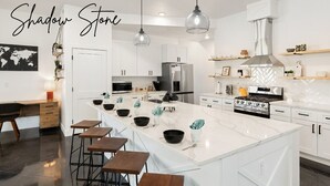 Une cuisine moderne avec des meubles blancs, un grand îlot central doté de tabourets, des appareils en acier inoxydable et un éclairage suspendu.
