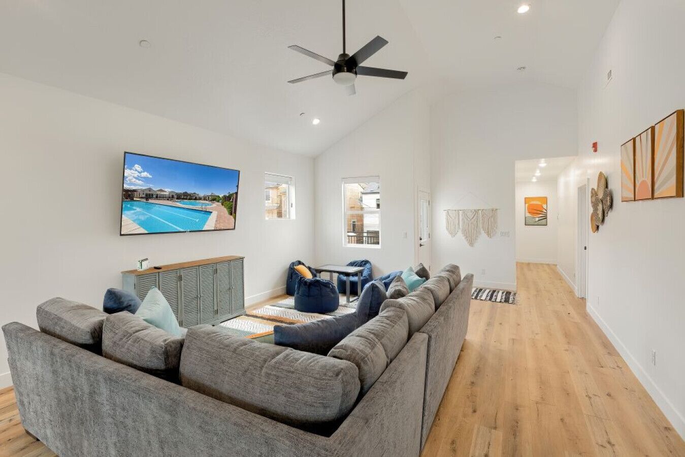 A modern living room with a grey sectional sofa, a flat-screen TV, and a ceiling fan.