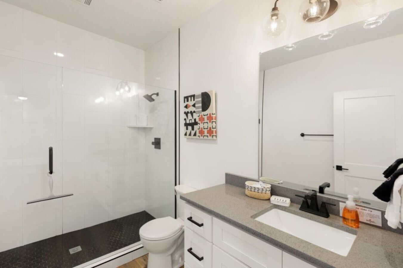 A modern bathroom with a glass shower enclosure, a toilet, a vanity with a mirror, and a sink.