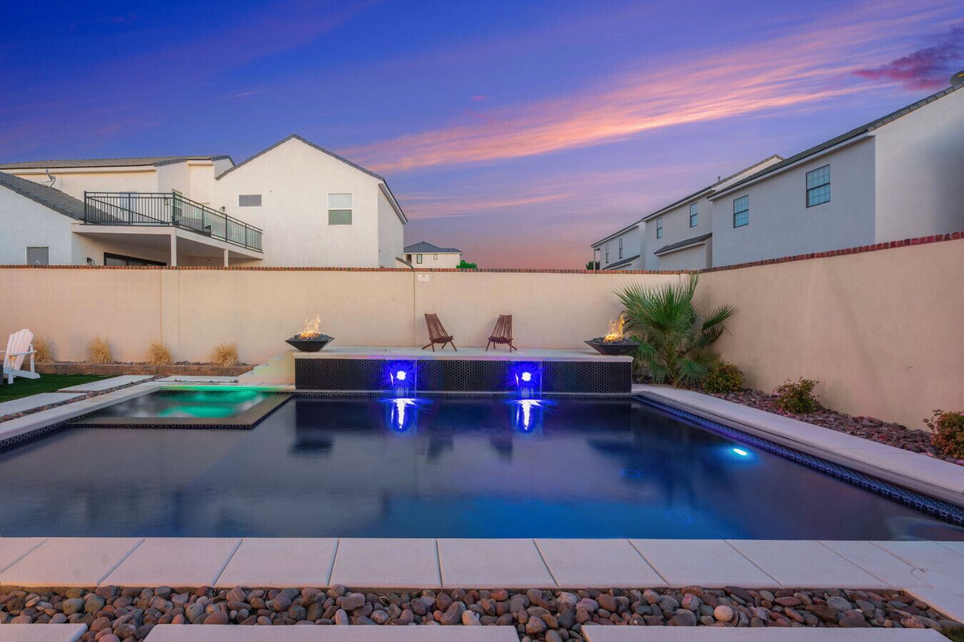 A rectangular swimming pool with a built-in hot tub and LED lights, surrounded by a patio area with seating and a view of adjacent buildings.
