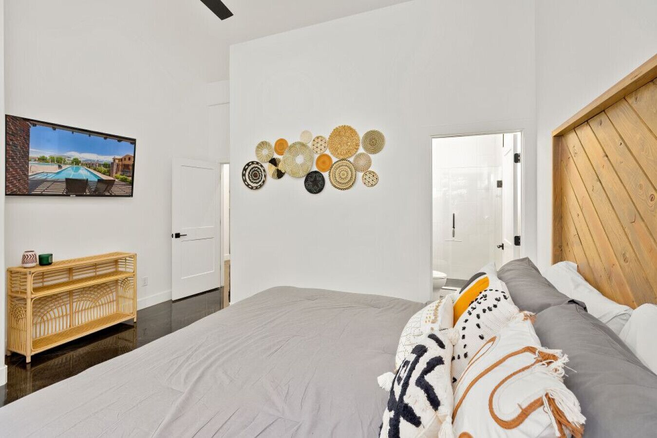 A modern bedroom with a large bed, a wooden headboard, a wall-mounted mirror, and a wall art piece.