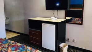 Una habitación de hotel pequeña con una cama, un escritorio con refrigerador, televisión y espejo.