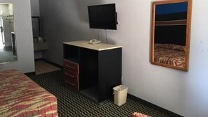 Habitación de hotel con cama, escritorio, silla, televisor y espejo en la pared.