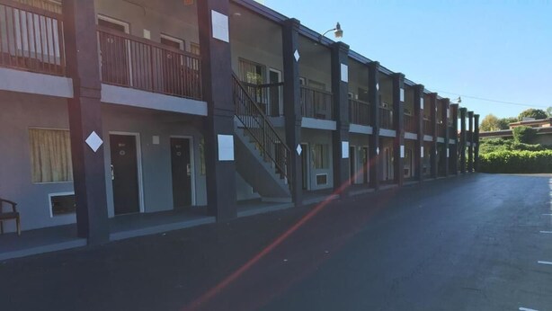 Un hotel de varios pisos con balcones, una escalera central y un estacionamiento.
