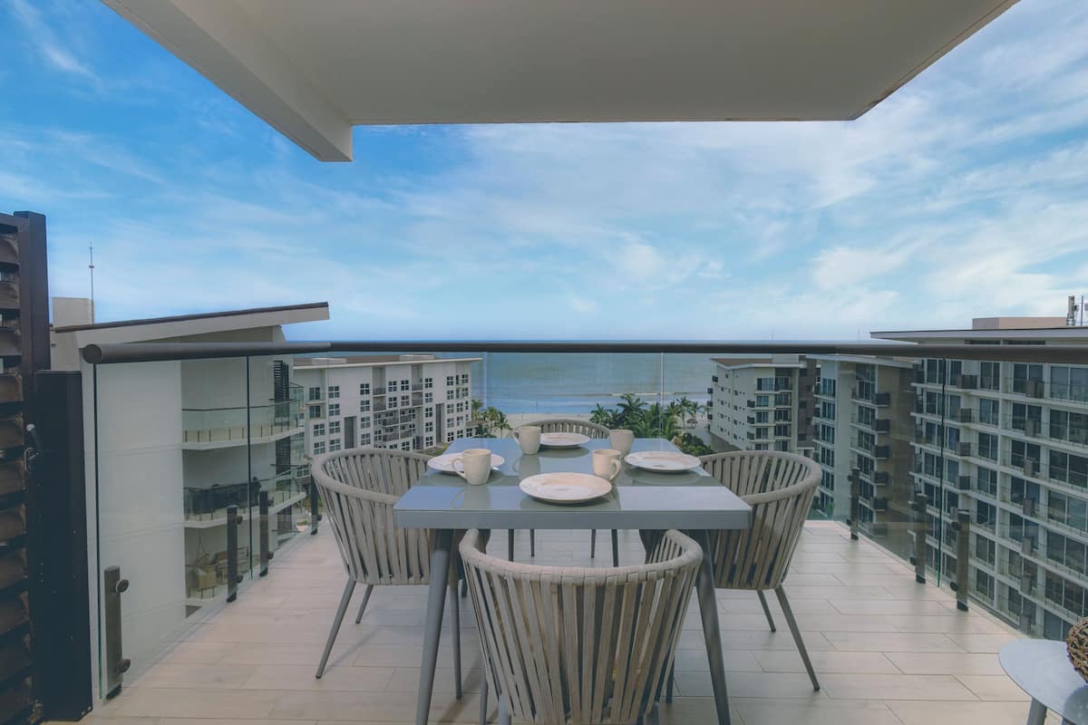 Un balcon avec une table dressée pour quatre personnes, offrant une vue sur la ville et la mer.