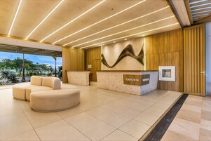 Una zona de recepción moderna con un espacio de estar curvo, un mostrador de recepción que dice "TOUR DESK" y una pieza decorativa en la pared.